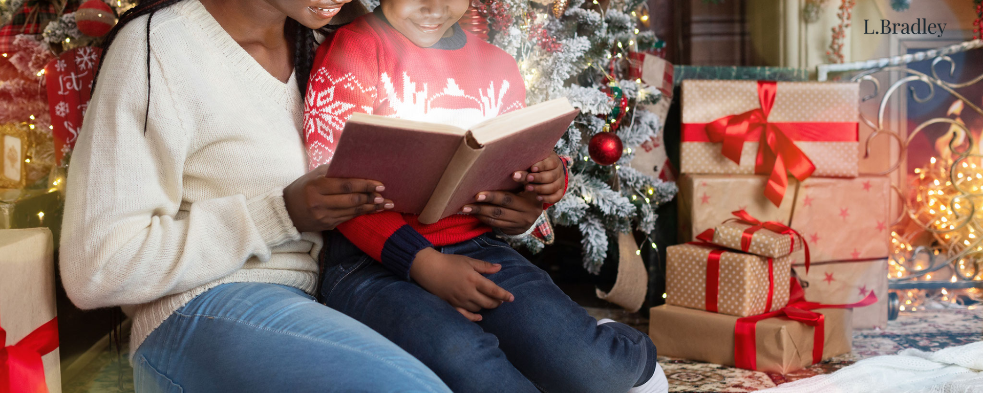 woman and child reading book in front of christmas tree and presents.